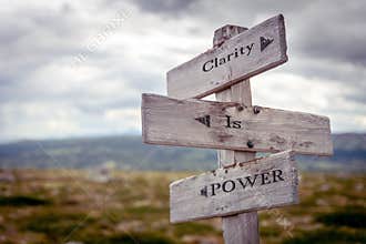 clarity is power text engraved on old wooden signpost outdoors in nature