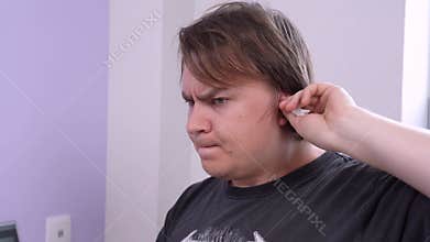 Man with angry face expression inserts the curled paper swabs into his ears