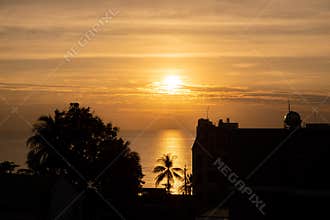 Sunset over the sea in the tropics, sunset sun in the clouds, in the foreground the contours of palm trees