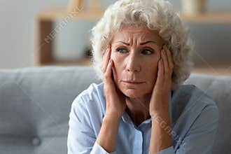 Close up worried elderly 70s woman deep in sad thoughts