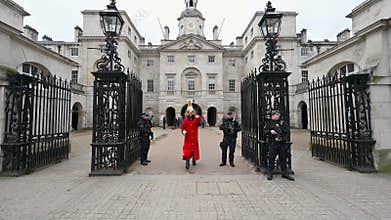 A trooper of the Household Cavalry in full traditional red uniform and holding a sword, marches towards camera and comes to
