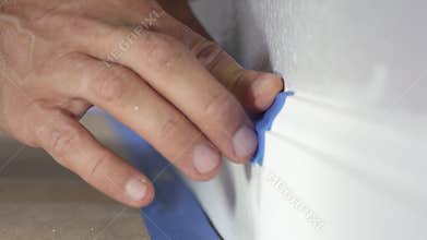Painter Using Masking Blue Tape to Secure Baseboard, Moulding. Preparation For Room Painting