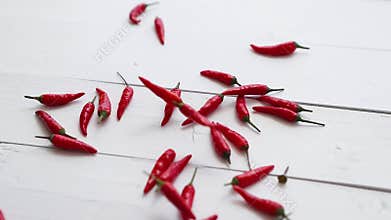 Freely falling small red chilli peppers on the white wooden table. Slow motion video