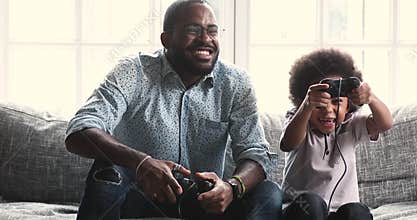 Happy african american father playing video games with little son.