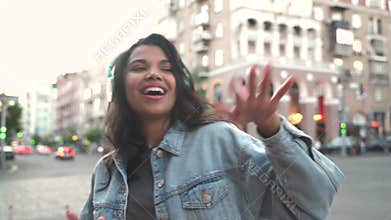 Happy funky cool African American girl wearing headphones dancing on street.