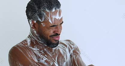 Smiling handsome biracial man enjoying skincare showering routine in bathroom.