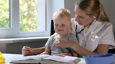 Doctor examining a child patient by stethoscope while watching book together. cute boy at pediatrician appointment