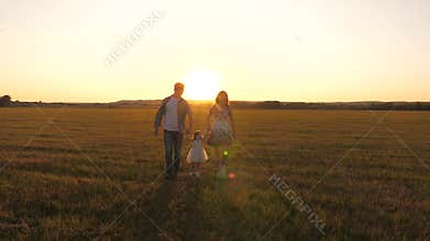 Little daughter holds mom and dad by hands and jumps on meadow in park in rays of yellow sun. Family happiness. healthy