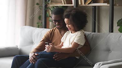Happy kid girl holding phone sit on african dad lap