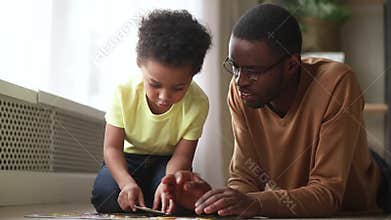 Happy cute little son playing with black dad assembling puzzle