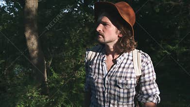 A young peasant walking in the woods. Hiker hiking in forest at sunset. Active lifestyle. Wearing a checkered shirt and
