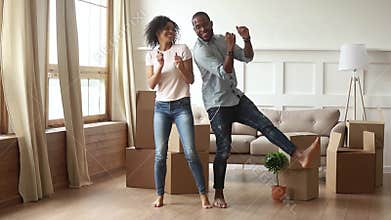 African couple first time home buyers dancing in living room