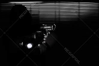Burglary and robbery. skillful professional masked burglar holding a gun and torch and breaking into the house, hand close up on