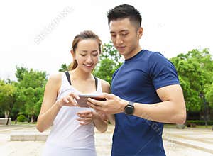 fitness couple wearing sportswear and looking at smartphone