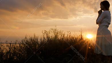 Silhouette of young woman figure praying to God at sunset, the girl folded her hands at the chin in the field, concept of religion