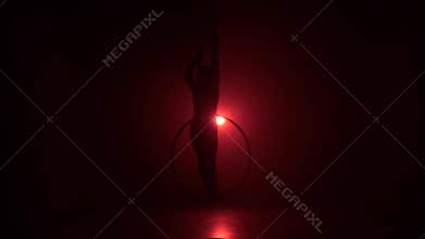 Silhouette Aerial acrobat in the ring. A young girl performs the acrobatic elements in the air ring on red background