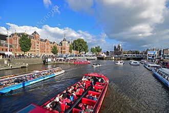 High traffic of passing boat canal Cruises filled with mass tourists on river canal with Amsterdam Central Station