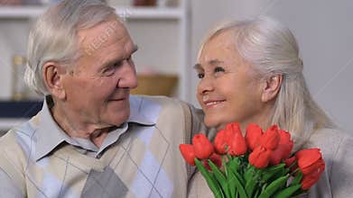 Happy senior woman with bunch of flowers embracing husband, everlasting love