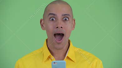 Face of happy handsome bald businessman using phone and looking surprised