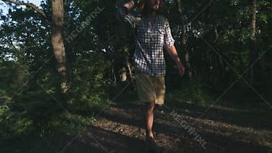 A young peasant walking in the woods. Hiker hiking in forest at sunset. Active lifestyle. Wearing a checkered shirt and