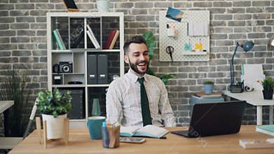 Happy employee using laptop then raising arms celebrating success in office