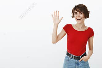 Hey whats up. Attractive sociable cheerful friendly european girl short haircut waving raised palm say hi hello greeting