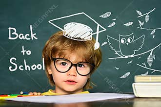 Cute little preschool kid boy in a classroom. Blackboard background. Teachers day. Kids from primary school. September 1