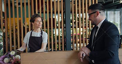 Slow motion of joyful guy paying for bunch of flowers with credit card in shop