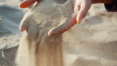 SLOW MOTION, CLOSE UP: The sand passes through the fingers of a young woman. The sand is running through fingers of a