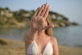 Girl in the beach with his hand raised up in a stop gesture