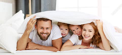 Happy family mother, father and children laughing, playing and smiling in bed   at home