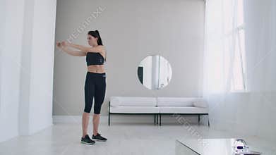 Brunette female does warm-up and exercises in her apartment in the morning, turns the body blindly and right with arms