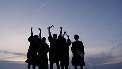 Silhouette of Diverse International Students Celebrating Graduation Tossing Caps in the air.