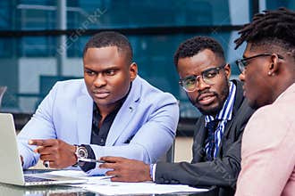 A group of three stylish African American men entrepreneurs in fashion business suits working sitting at table with