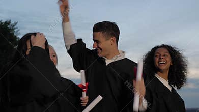 Happy and excited mixed ethnicity group of student friends on graduation day toss hats in the air while walking..