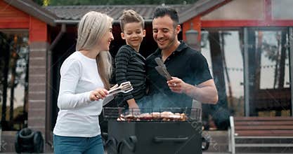 Happy family cook meat on grill. Father and mother with son fry sausages on grill and smiling. Slow motion
