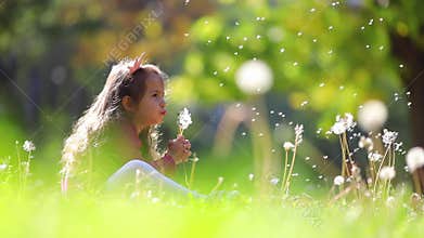 Cute little girl blowing  dandelions in autumn park. Wishes, dreams, playtime.
