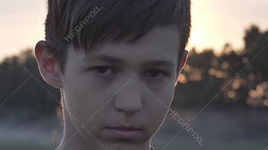 Portrait of offended sad boy in a wheat field looking at the camera at sunset close up