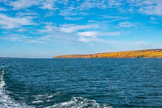Wide angle view of the Apostle Islands in Fall, as seen from a boat. Wake of boat in photo, trees in the autumn