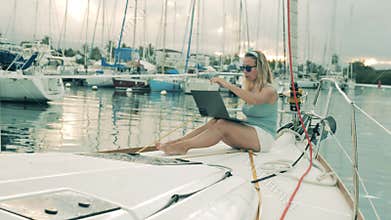 One woman sits on a yacht, working with laptop.