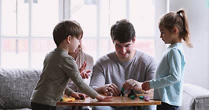 Cheerful young parents and small kids sculpting play dough at home