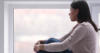 Thoughtful lonely african woman sit on sill look through window