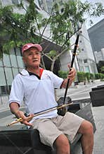 A senior playing a Chinese two-stringed fiddle against the modern city backdrop