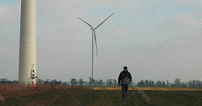 A man Walks In A Field On Background Rotating Windmill. The Power Of The Wind. A Clean And Renewable Energy Solution. Wind Turbine