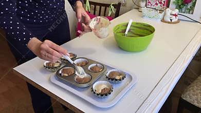 Woman puts dough with cocoa in muffin baking dish. The forms already contain a little light dough