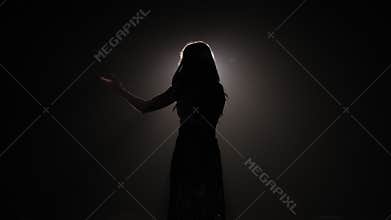 Silhouette of a beautiful girl on stage with concert lighting in a evening dress
