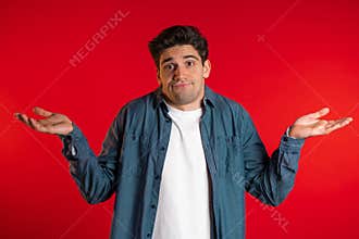 Young handsome unsure guy in denim shirt shrugs his arms, makes gesture of I don`t know, can`t help anything