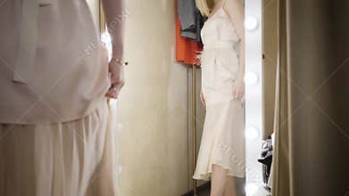 Young Caucasian woman trying on elegant dress in dressing room. Camera moving down, wealthy lady in beige outfit and