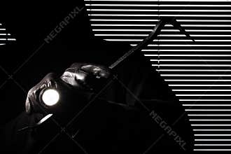 Burglary and robbery. skillful professional masked burglar holding a torch and crowbar and breaking into the house, hand close up