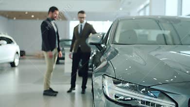 Handsome guy talking to sales agent in car dealership, focus on expensive automobile. Focus on car headlight